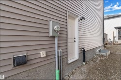 Exterior wall featuring horizontal siding in a neutral tone, a white service door with a dark handle, an exterior light fixture, and a foundation with a parge coat finish - 