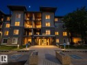 Multi-story residential building featuring stone and siding exterior accents, multiple private balconies with railings, and a prominent illuminated main entrance - #107 530 Watt Bv Sw, Edmonton, AB  - Outdoor 
