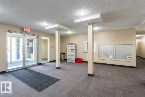 Building entryway featuring glass doors, patterned carpet flooring, and a wall-mounted mailbox system - #107 530 Watt Bv Sw, Edmonton, AB - Indoor Photo Showing Other Room