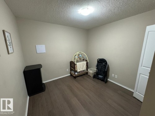 Neutral-toned room featuring wood-finish flooring, white baseboards, and a white interior door - #107 530 Watt Bv Sw, Edmonton, AB - Indoor