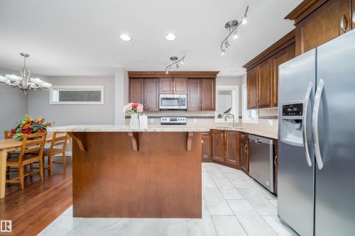 Kitchen featuring dark wood-finish cabinetry, stainless steel appliances, light-toned countertops, tile flooring, and a central island with bar seating - 11342 79 Avenue, Edmonton, AB - Indoor Photo Showing Kitchen