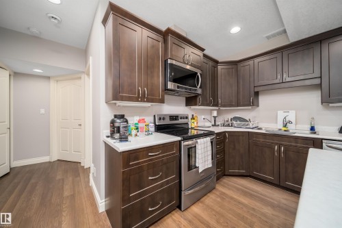 Well-appointed kitchen featuring wood-finish flooring, dark wood cabinetry, white countertops, stainless steel appliances, and recessed lighting - 11342 79 Avenue, Edmonton, AB - Indoor Photo Showing Kitchen With Stainless Steel Kitchen With Double Sink