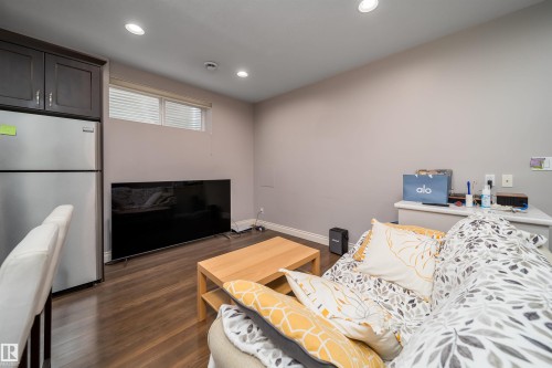 Living area featuring wood-finish flooring, recessed lighting, and a stainless steel refrigerator with dark cabinetry - 11342 79 Avenue, Edmonton, AB - Indoor