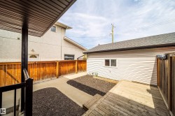 Rear property area featuring a wooden deck, concrete pathway, and decorative ground cover - 