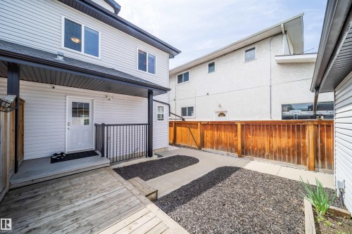 Rear exterior featuring a covered porch with black railings, light-colored siding, and a wooden deck - 11342 79 Avenue, Edmonton, AB - Outdoor With Deck Patio Veranda With Exterior