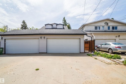Detached garage structure featuring two overhead doors, light-colored siding, and a dark shingled roof with decorative dormers - 11342 79 Avenue, Edmonton, AB - Outdoor