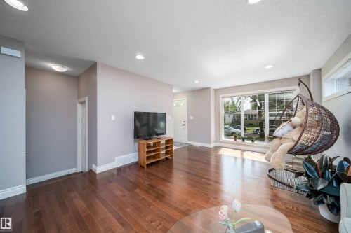 Spacious living area featuring rich wood-finish flooring, abundant natural light from a large picture window, recessed ceiling lighting, and a neutral wall color palette - 11342 79 Avenue, Edmonton, AB - Indoor Photo Showing Living Room