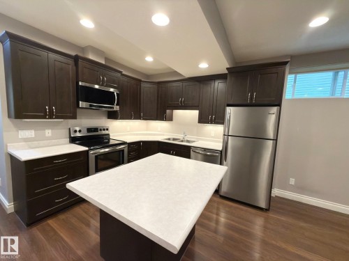 Modern kitchen featuring dark wood-finish cabinetry, stainless steel appliances, a center island with a light-toned countertop, and recessed lighting - 11342 79 Avenue Nw, Edmonton, AB - Indoor Photo Showing Kitchen With Stainless Steel Kitchen With Double Sink With Upgraded Kitchen