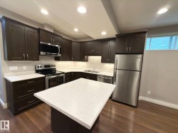 Modern kitchen featuring dark wood-finish cabinetry, stainless steel appliances, a center island with a light-toned countertop, and recessed lighting - 