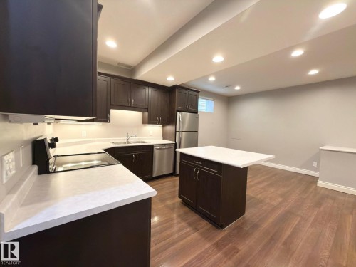 Dark wood-finish cabinetry, light-toned countertops, stainless steel appliances, kitchen island, and wood-finish flooring - 11342 79 Avenue Nw, Edmonton, AB - Indoor Photo Showing Kitchen With Double Sink