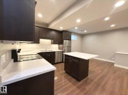 Dark wood-finish cabinetry, light-toned countertops, stainless steel appliances, kitchen island, and wood-finish flooring - 