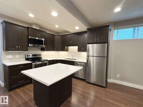 Kitchen featuring dark wood-finish cabinetry, stainless steel appliances, a center island with a white countertop, and wood-finish flooring - 11342 79 Avenue Nw, Edmonton, AB - Indoor Photo Showing Kitchen With Stainless Steel Kitchen With Double Sink