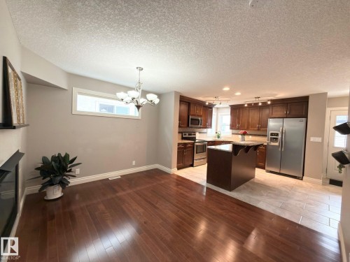 Open-concept living space featuring wood-finish flooring, a contemporary chandelier, a kitchen with dark wood cabinetry, a center island, and stainless steel appliances - 11342 79 Avenue Nw, Edmonton, AB - Indoor Photo Showing Kitchen