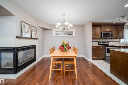 Dining area featuring wood-finish flooring, a contemporary chandelier, and a gas fireplace with a tiled surround - 11342 79 Avenue, Edmonton, AB - Indoor With Fireplace