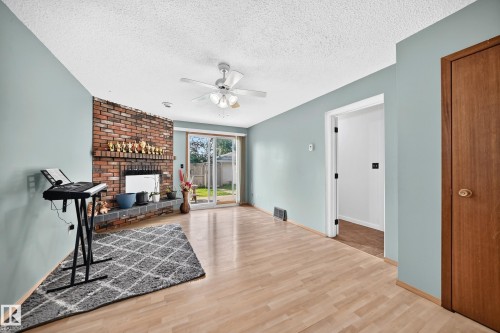 Living area featuring wood-finish flooring, a brick fireplace with hearth, and light blue wall color - 1928 68 Street Nw, Edmonton, AB - Indoor With Fireplace