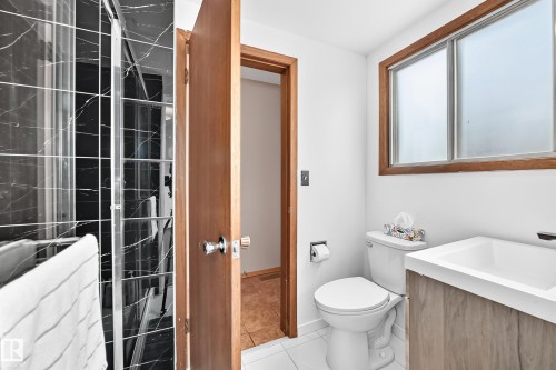 Bathroom featuring a shower with black marble-patterned tile, a white toilet, and a vanity with a white basin and wood-finish cabinetry - 1928 68 Street Nw, Edmonton, AB - Indoor Photo Showing Bathroom