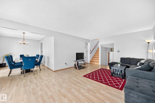 Bright open-concept living area featuring light wood-finish flooring, neutral wall tones, a dining space with chandelier lighting, and a staircase with wood treads and a wood handrail - 1928 68 Street Nw, Edmonton, AB - Indoor Photo Showing Living Room