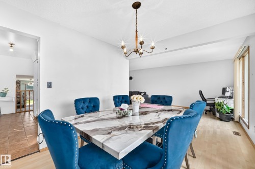 Dining area featuring light wood-finish flooring, a contemporary chandelier, and a large window with vertical blinds - 1928 68 Street Nw, Edmonton, AB - Indoor Photo Showing Dining Room