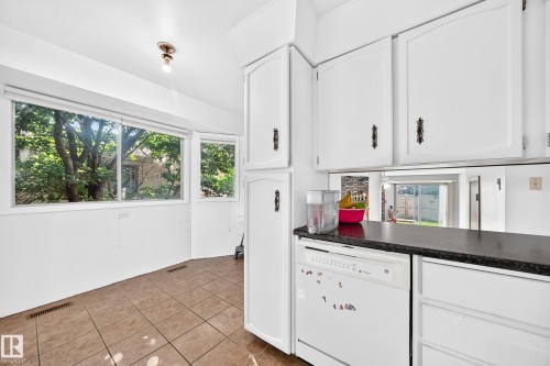 Kitchen space featuring white cabinetry, a black countertop, and a white built-in dishwasher - 1928 68 Street Nw, Edmonton, AB - Indoor Photo Showing Kitchen