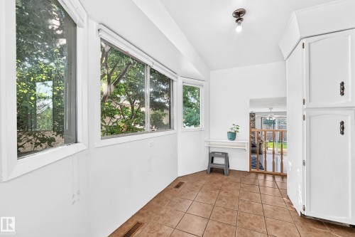 Room featuring multiple white-framed windows, tile flooring, built-in white cabinetry, a built-in wall shelf, and a recessed entryway with a wooden railing - 1928 68 Street Nw, Edmonton, AB - Indoor Photo Showing Other Room