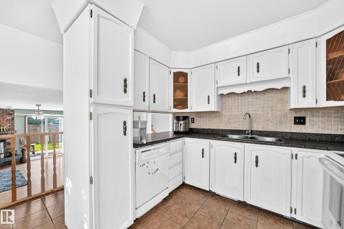 Kitchen featuring white cabinetry with decorative hardware, dark stone-finish countertops, and a full tile backsplash - 1928 68 Street Nw, Edmonton, AB - Indoor Photo Showing Kitchen With Double Sink