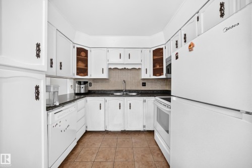 Kitchen featuring white cabinetry with dark hardware, dark countertops, and tile flooring - 1928 68 Street Nw, Edmonton, AB - Indoor Photo Showing Kitchen With Double Sink