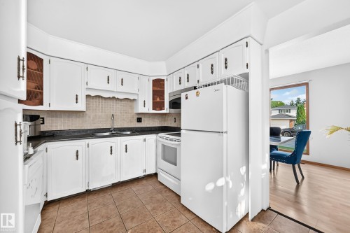 Kitchen featuring white cabinetry, dark countertops, a tile backsplash, and ceramic tile flooring - 1928 68 Street Nw, Edmonton, AB - Indoor Photo Showing Kitchen With Double Sink