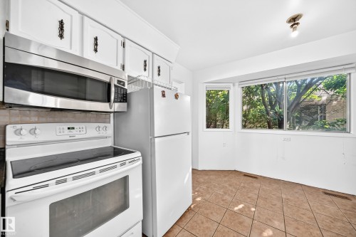 Kitchen featuring white cabinetry with decorative hardware, a stainless steel over-the-range microwave, and a white electric range - 1928 68 Street Nw, Edmonton, AB - Indoor Photo Showing Kitchen