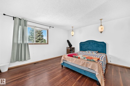 Bedroom featuring wood-finish flooring, white walls, and a window with a green tree backdrop - 1928 68 Street Nw, Edmonton, AB - Indoor Photo Showing Bedroom