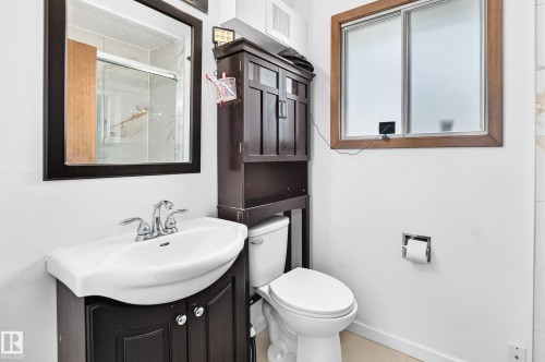 Bathroom featuring a wood-finish framed mirror, a vanity with a white ceramic sink, a chrome faucet, a toilet, and a wood-frame window with frosted glass - 1928 68 Street Nw, Edmonton, AB - Indoor Photo Showing Bathroom