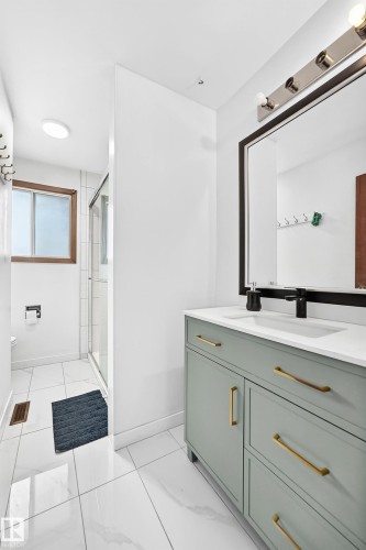 Modern bathroom vanity featuring light green cabinetry with gold-toned hardware, a white countertop, and a black-framed mirror - 1928 68 Street Nw, Edmonton, AB - Indoor Photo Showing Bathroom