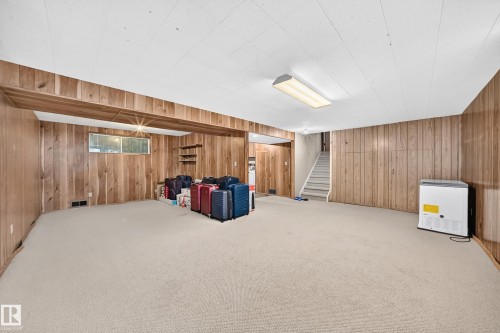 Spacious room featuring wood paneling, light-colored carpeting, and a drop ceiling with fluorescent lighting - 1928 68 Street Nw, Edmonton, AB - Indoor