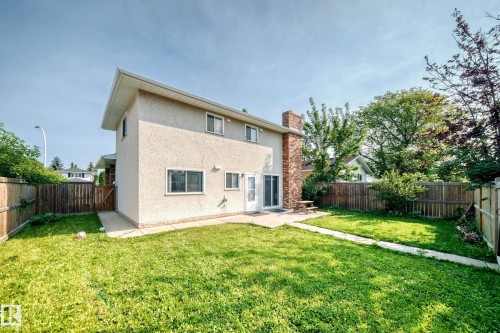 Expansive backyard featuring a manicured lawn, full privacy fencing, and a concrete patio area with sliding glass door access to the residence - 1928 68 Street Nw, Edmonton, AB - Outdoor
