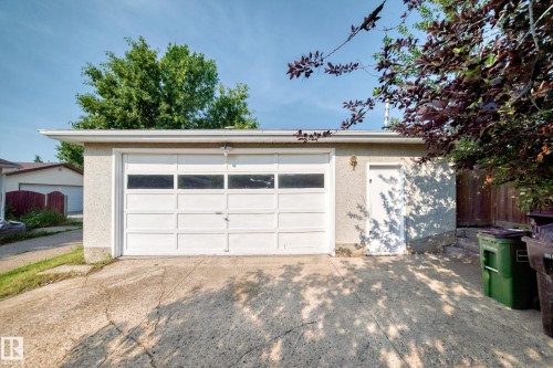 Detached garage with a white panel door and upper window inserts, featuring a side access door and stucco exterior - 1928 68 Street Nw, Edmonton, AB - Outdoor