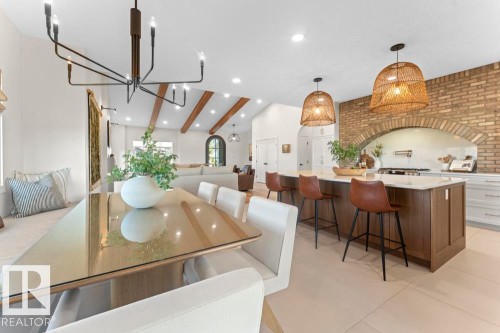 Open-concept living space featuring a central kitchen island with seating, exposed brick archway, lighting, and vaulted ceilings with exposed beams - 2503 Lockhart Way, Cold Lake, AB - Indoor Photo Showing Dining Room