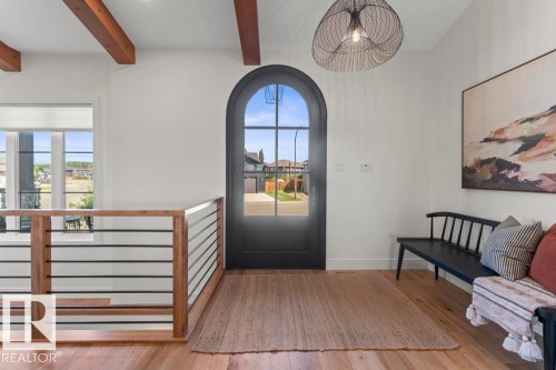 Arched entryway door with glass paneling, hardwood flooring, exposed ceiling beams, contemporary chandelier, and modern railing with wood and metal accents - 2503 Lockhart Way, Cold Lake, AB - Indoor Photo Showing Other Room