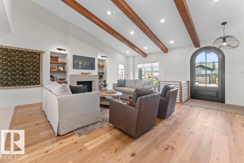 Spacious living area featuring vaulted ceilings with exposed wood beams, a fireplace with fluted paneling and built-in shelving, hardwood flooring, lighting, and a prominent arched entryway - 2503 Lockhart Way, Cold Lake, AB - Indoor Photo Showing Living Room With Fireplace