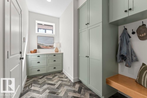 Entryway featuring herringbone-patterned tile flooring, built-in sage green cabinetry with black hardware, a light wood bench, and a transom window - 2503 Lockhart Way, Cold Lake, AB - Indoor Photo Showing Other Room