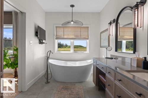 Freestanding soaking tub with floor-mounted faucet, vanity with undermount sinks, stone countertop, and wood-finish cabinetry - 2503 Lockhart Way, Cold Lake, AB - Indoor Photo Showing Bathroom