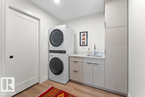Dedicated laundry space featuring stacked appliances, a utility sink, light gray cabinetry, a light countertop, and wood-finish flooring - 2503 Lockhart Way, Cold Lake, AB - Indoor Photo Showing Laundry Room