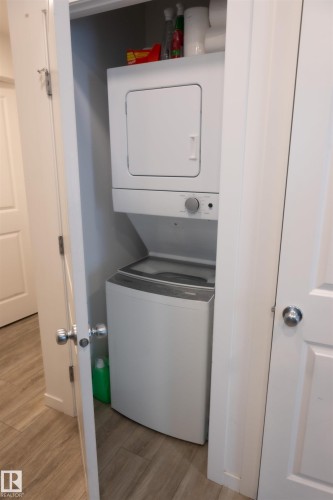 Dedicated laundry closet featuring a stackable white washer and dryer unit, and wood-finish flooring - #103 860 Secord Bv Nw, Edmonton, AB - Indoor Photo Showing Laundry Room