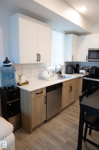 Modern kitchen featuring two-tone cabinetry with white upper cabinets and wood-finish lower cabinets, complemented by dark hardware - #103 860 Secord Bv Nw, Edmonton, AB - Indoor Photo Showing Kitchen