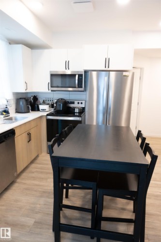 Modern kitchen featuring stainless steel appliances, light wood-finish lower cabinetry, white upper cabinetry, and wood-finish flooring - #103 860 Secord Bv Nw, Edmonton, AB - Indoor Photo Showing Kitchen