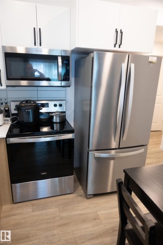 Contemporary kitchen featuring a stainless steel refrigerator, stainless steel range with ceramic cooktop, and an over-the-range microwave - #103 860 Secord Bv Nw, Edmonton, AB - Indoor Photo Showing Kitchen With Stainless Steel Kitchen