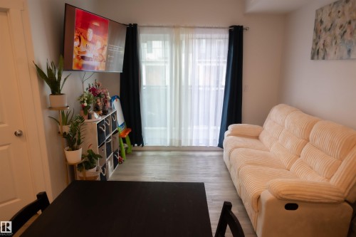 Living area with sliding glass door, sheer white curtains, and dark blue drapes - #103 860 Secord Bv Nw, Edmonton, AB - Indoor
