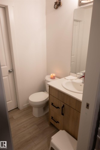 Modern bathroom vanity with wood-finish cabinetry, black hardware, and a white countertop with an integrated sink - #103 860 Secord Bv Nw, Edmonton, AB - Indoor Photo Showing Bathroom