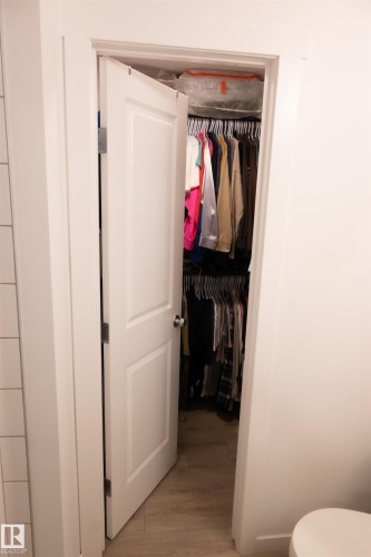Walk-in closet featuring wood-finish flooring and a white paneled door - #103 860 Secord Bv Nw, Edmonton, AB - Indoor Photo Showing Bathroom