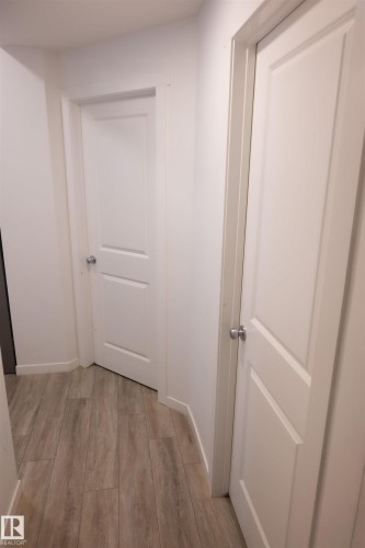 Hallway featuring wood-finish flooring, white paneled doors, and contemporary silver-toned hardware - #103 860 Secord Bv Nw, Edmonton, AB - Indoor Photo Showing Other Room