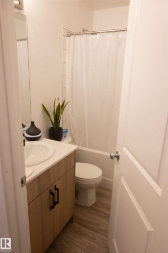 Bathroom featuring a light wood-finish vanity with a white countertop and integrated sink, complementing the wood-finish flooring - #103 860 Secord Bv Nw, Edmonton, AB - Indoor Photo Showing Bathroom
