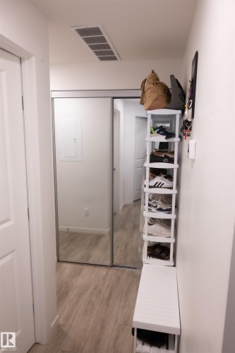 Hallway featuring wood-finish flooring, white doors, and a mirrored sliding closet door - #103 860 Secord Bv Nw, Edmonton, AB - Indoor Photo Showing Other Room